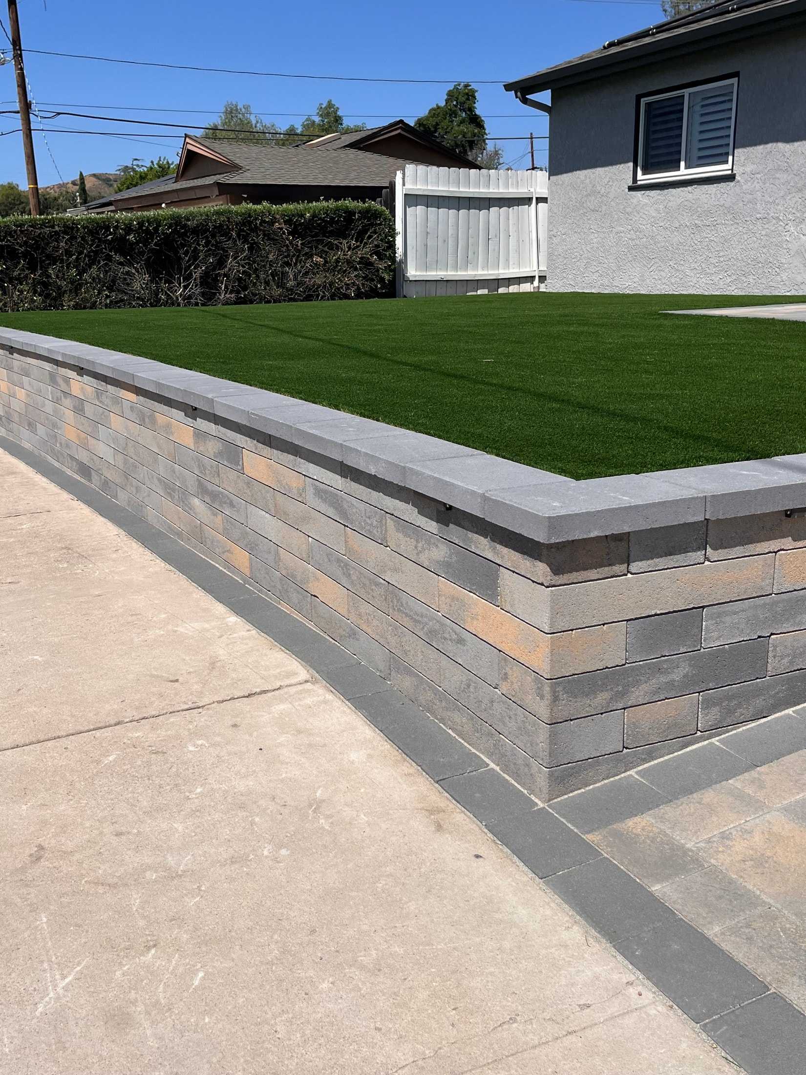 Gray and tan block wall with a smooth gray cap around a raised green lawn.