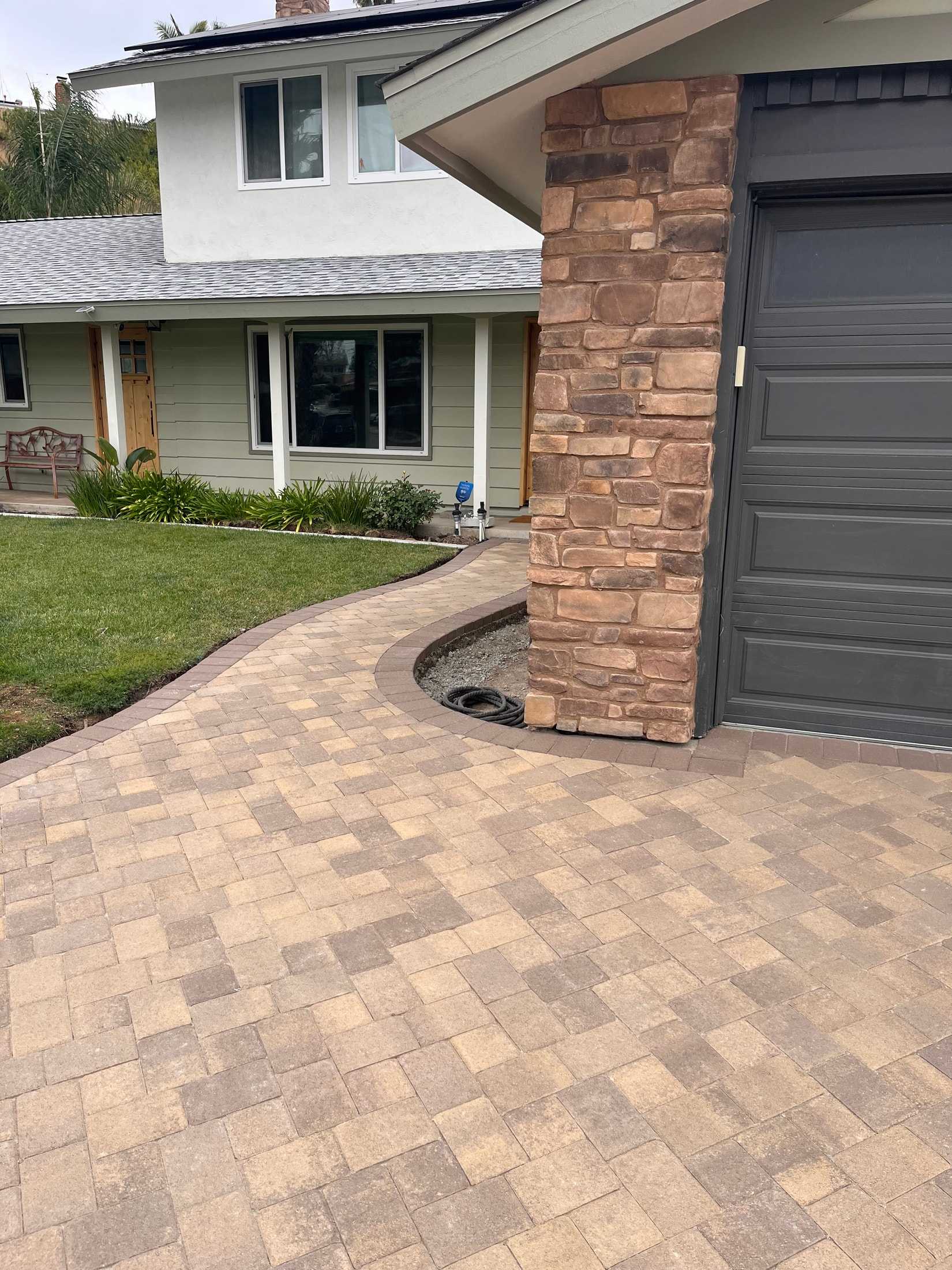 Curved paver walkway with a dark border connecting a driveway to the front entry beside a lawn.