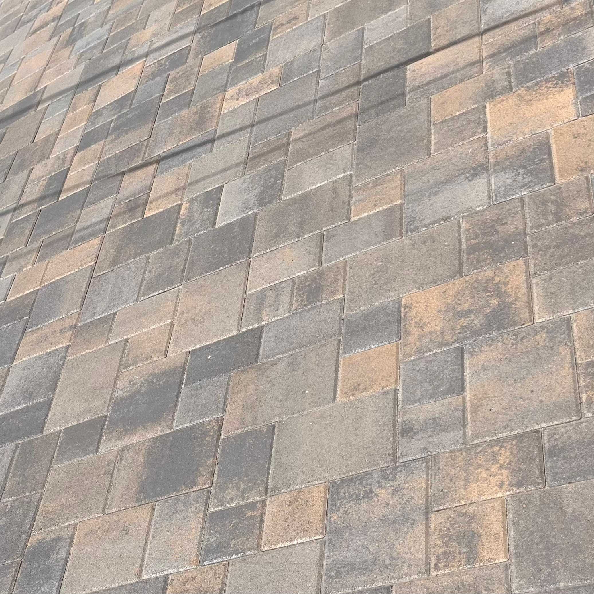 Close view of gray, charcoal, and tan rectangular pavers laid in a repeating pattern.