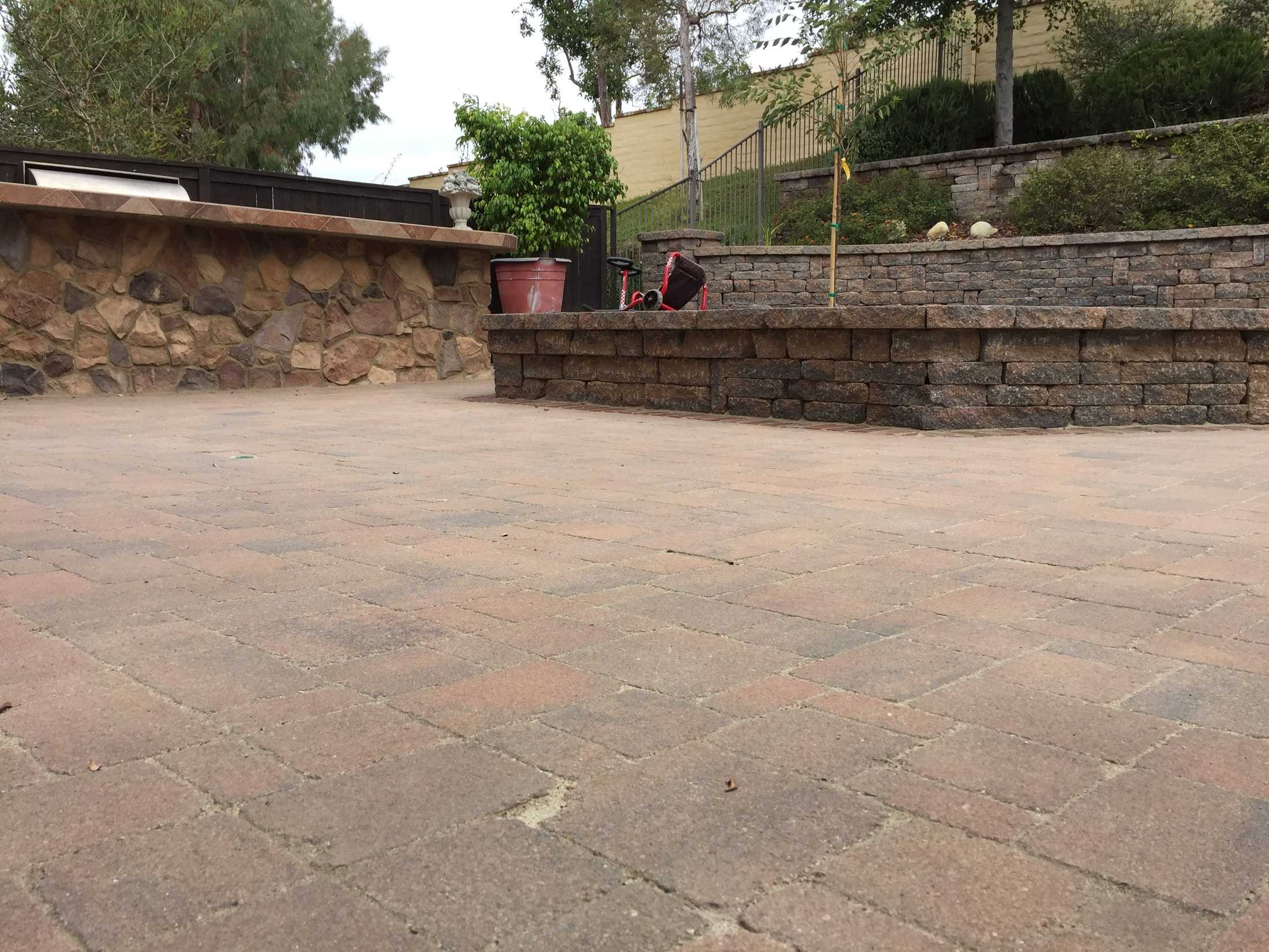 Earth-tone patio pavers beside a stone-faced counter and tiered block garden walls.