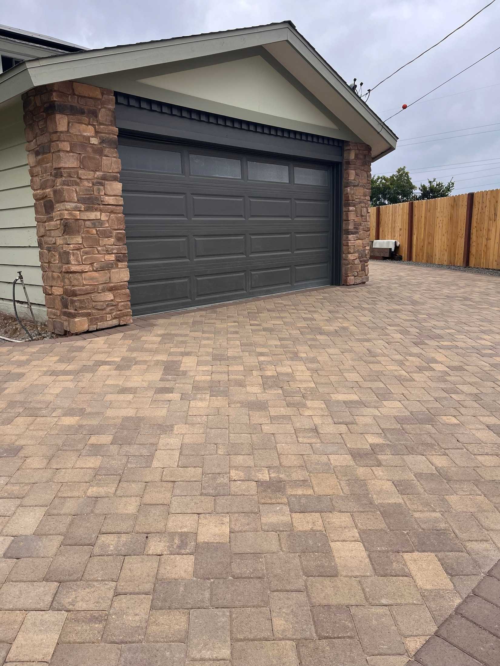 Tan and brown interlocking driveway pavers leading to a dark garage door with stone-faced columns.